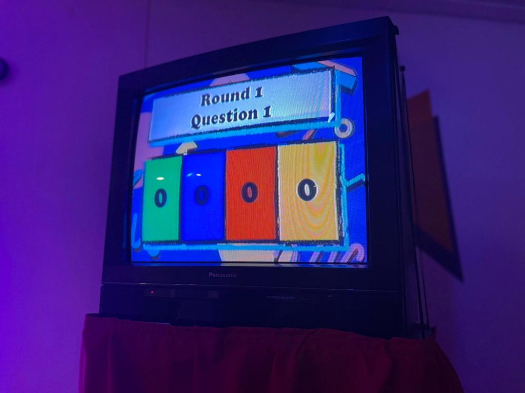 TV Screen indicating Round 1 Question 1 and showing the starting score of 0 in each of four colorful boxes.