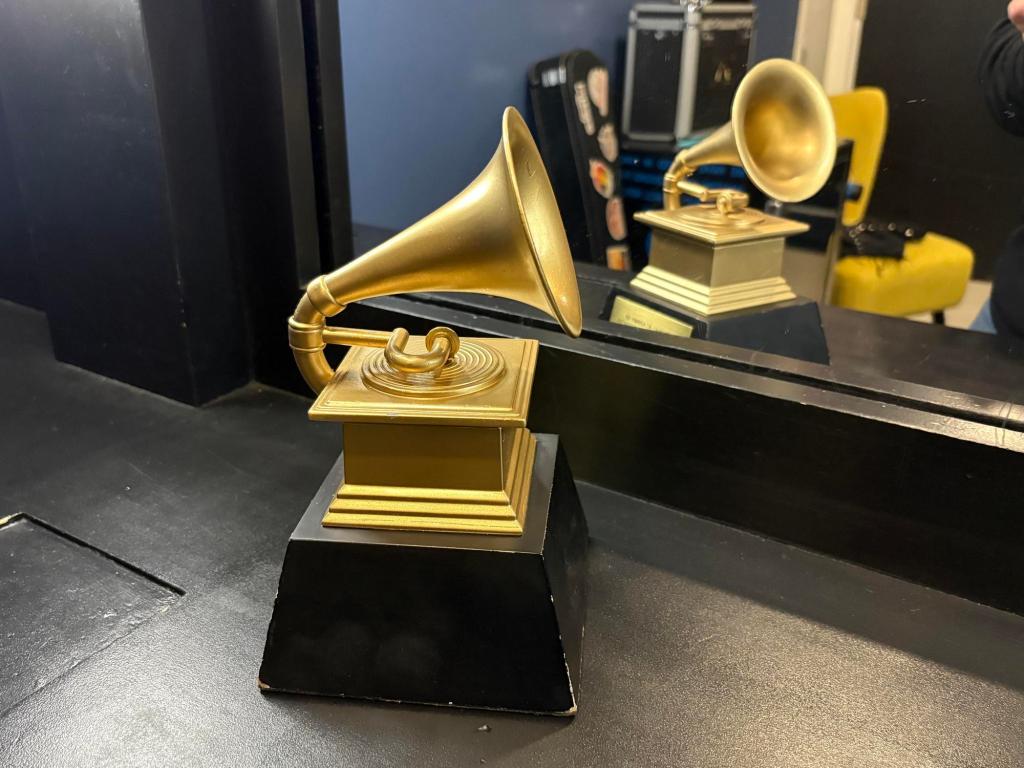 Closeup of a trophy, made up of a gold gramophone on a black base. It sits on a black surface and is reflected in the mirror behind it.