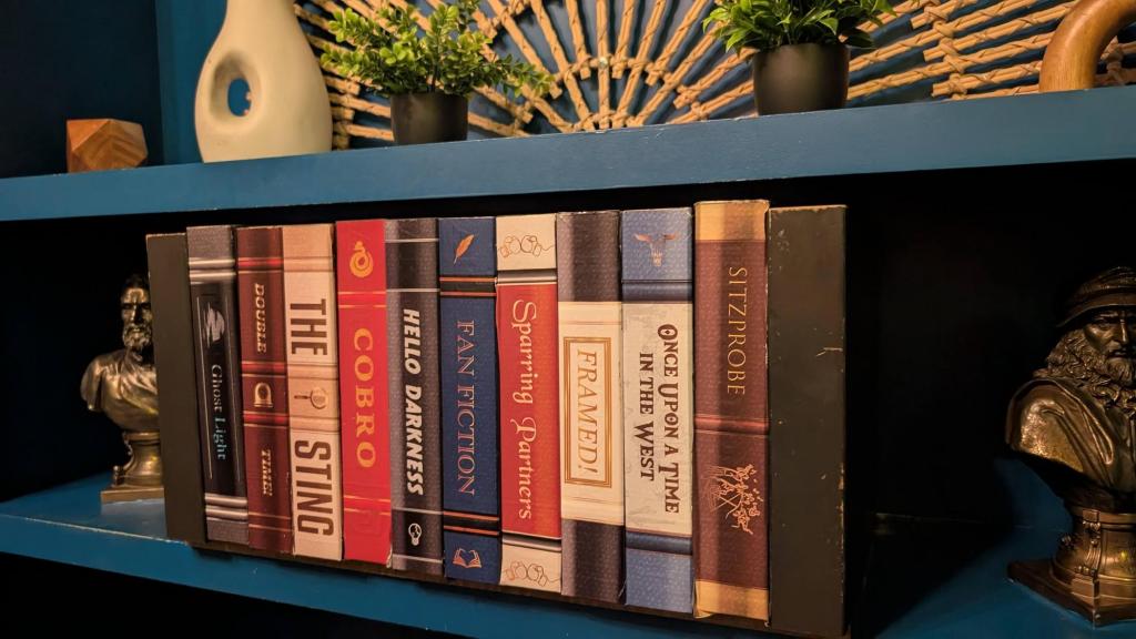 Two blue wall-mounted shelves. The upper one containing vases and knick-knacks and the lower containing a facade of books with busts on either side.