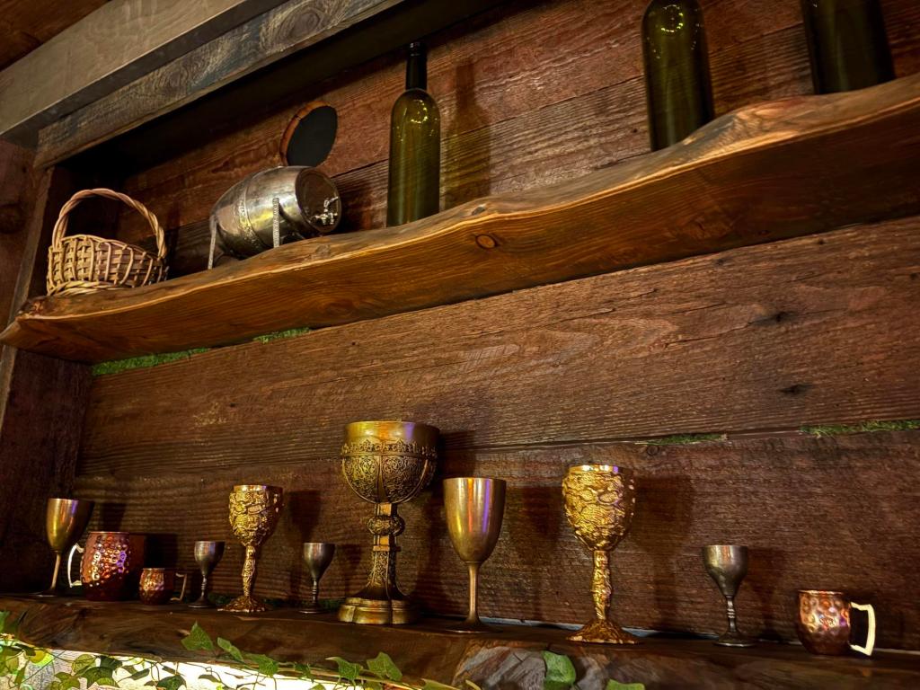 Closeup view of a wooden shelf decorated with ornate gold goblets, green wine bottles and a wicker basket.