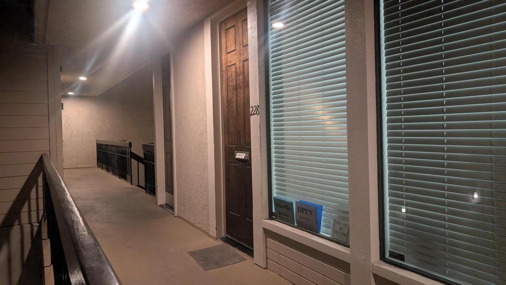 A non descript hallway with a closed door and windows with drawn blinds. Signs in the window show that Morillo Services is Open.