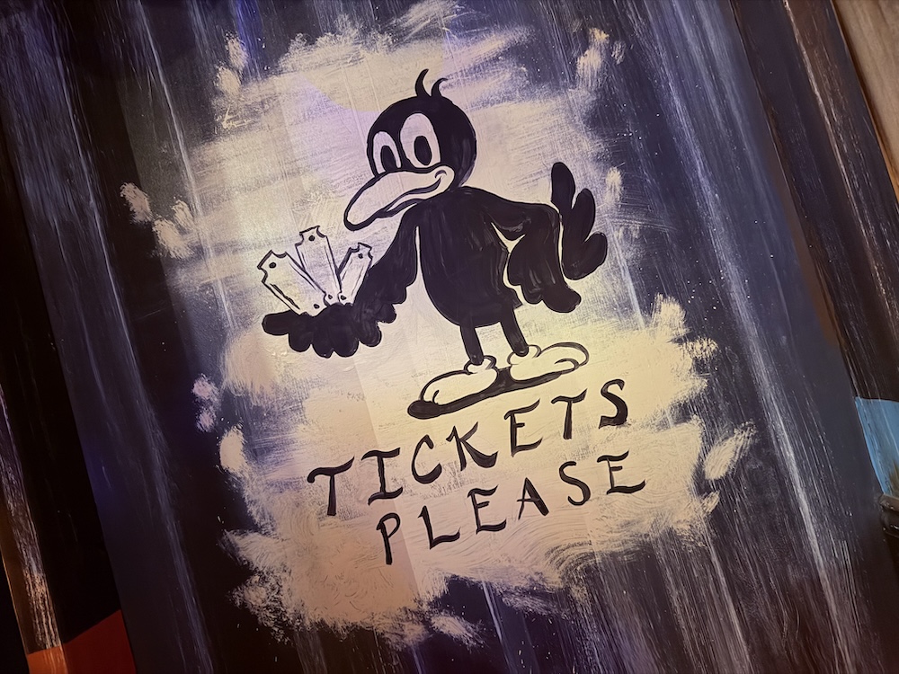 Closeup of a crow character reaching its wing out, holding tickets. Text reads, "Tickets Please"