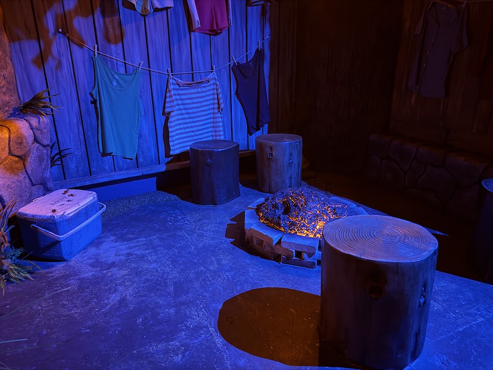 A smoldering fire outside of a camper. Clothing hangs on a line beyond.