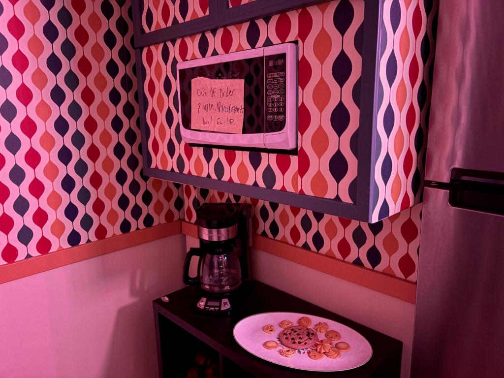 Corner of room with retro patterned wallpaper, a microwave, and below it, a coffee machine and plate of cookies.