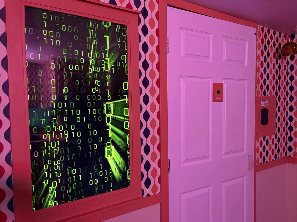 Closeup of a large vertical computer monitor on the wall, displaying a screen with black background and neon green 1s and 0s