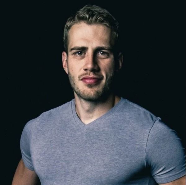 man with wavy blond hair in a v-neck grey t-shirt