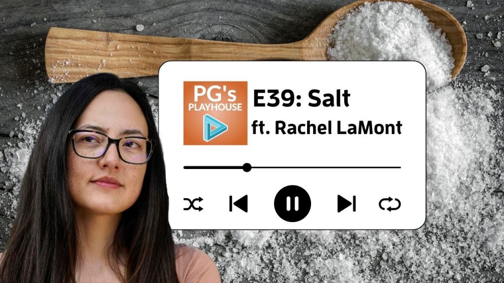 asian woman wearing glasses with freckles with long straight dark hair. salt spilled on a table in the background with wooden spoon filled with salt