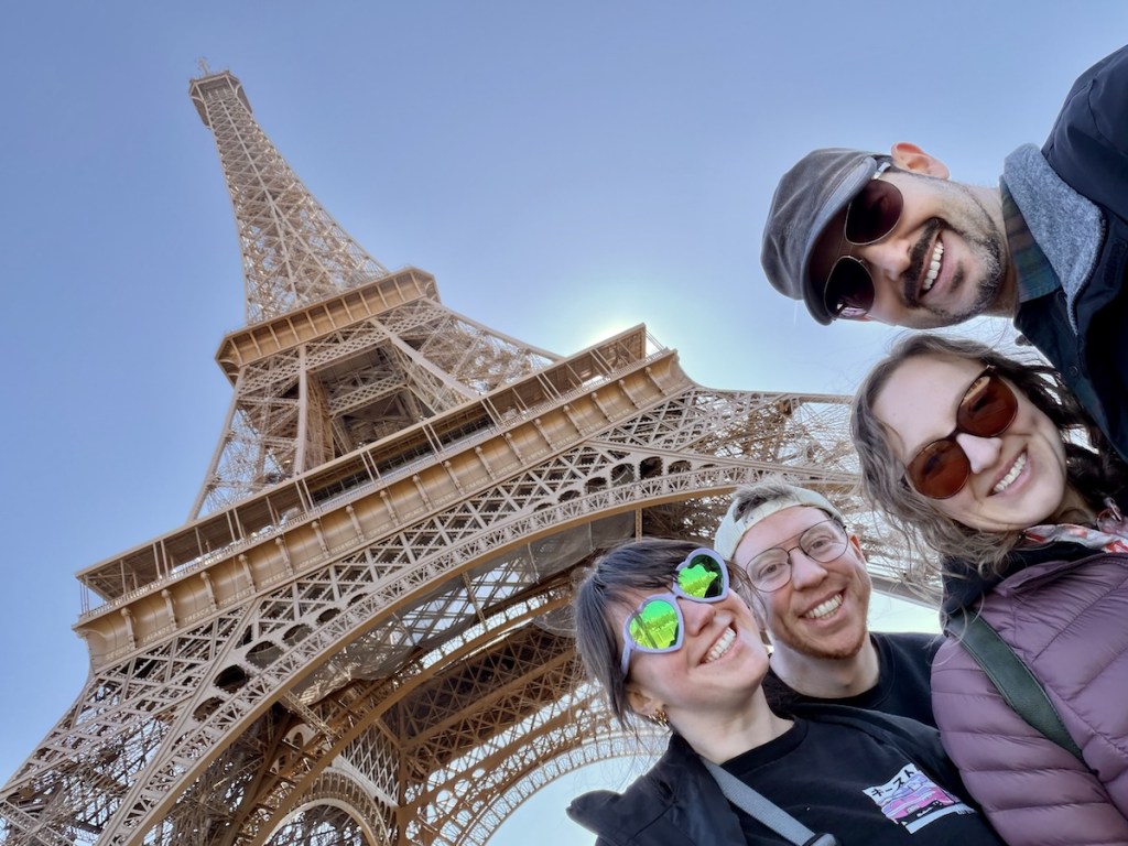 Theresa, Ryan, Lisa, and David taking an upwards angled selfie in front of the Eiffle Tower on a beautiful day.