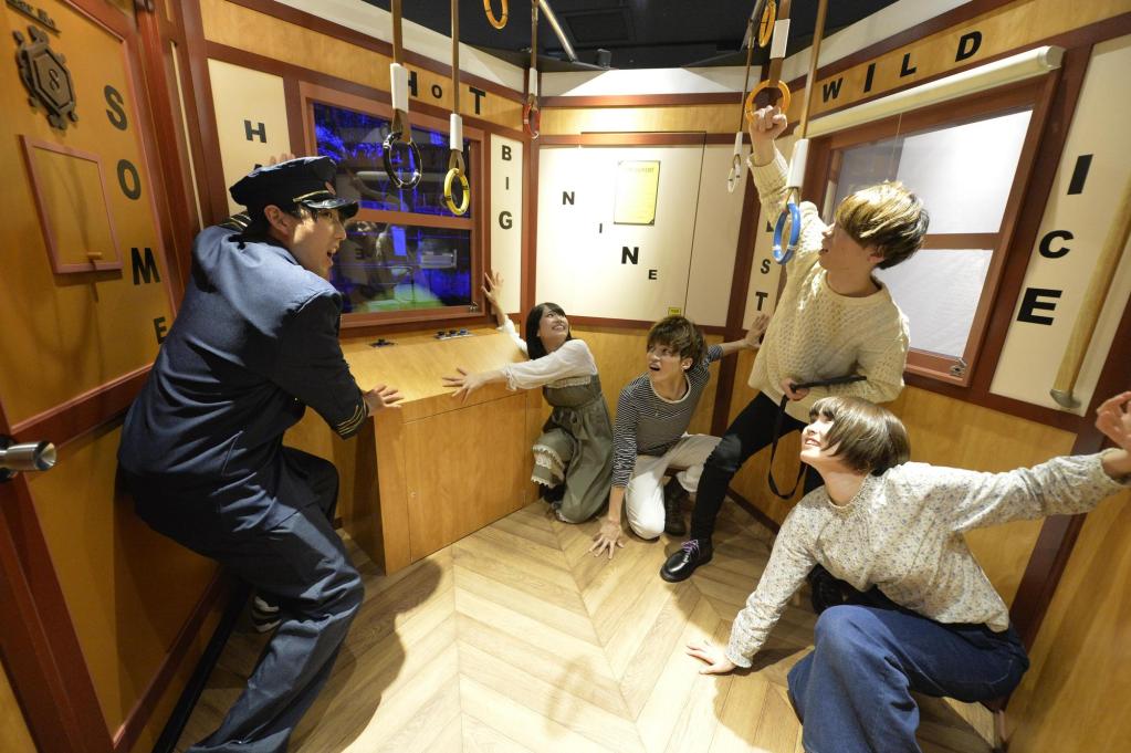 A train car with handles dangling from the ceiling and various words written on the walls, with a train employee and passengers bracing for impact