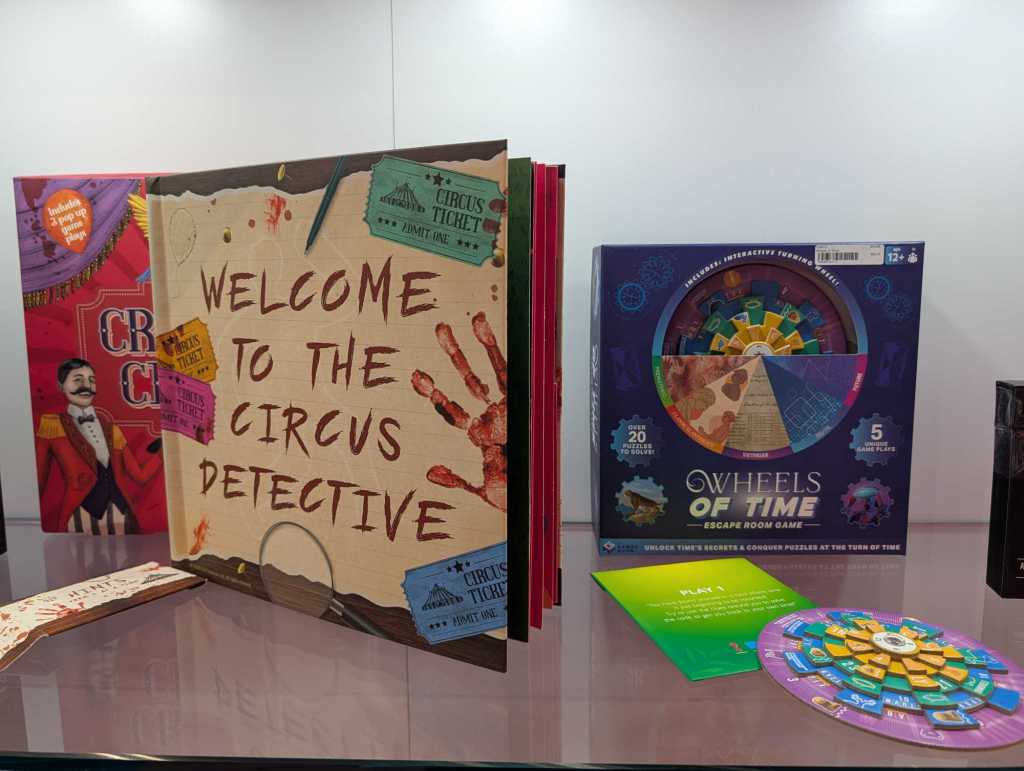 close up of two boxed games, one a horror circus pop-up book, the other called Wheels of Time