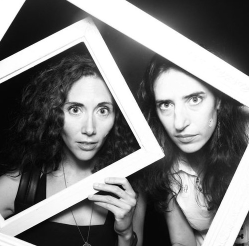 black and white image of two women holding white frames around their faces. both have large eyes, with dark curly hair.