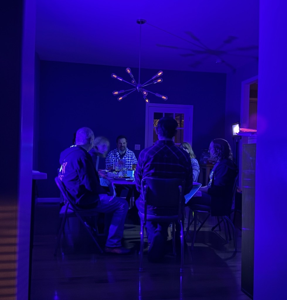 A group of people sitting around a dining room table in a room lit by black light.