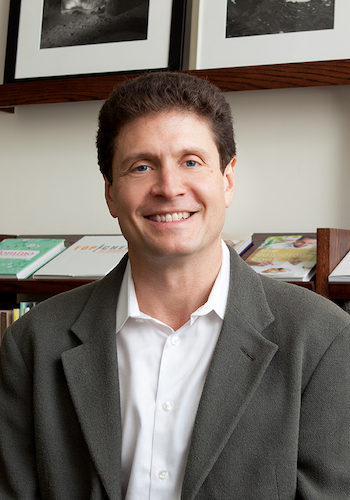 Man in early 60's with blue eyes, brown wavy hair in grey suit and loosely buttoned white shirt