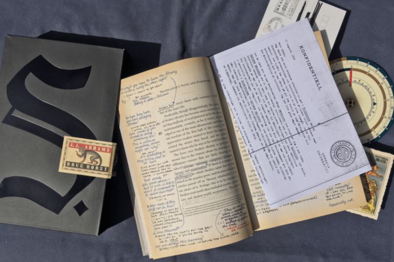 book open with writing in margins. Scattered around is a decoder ring, postcard, and typewritten papers