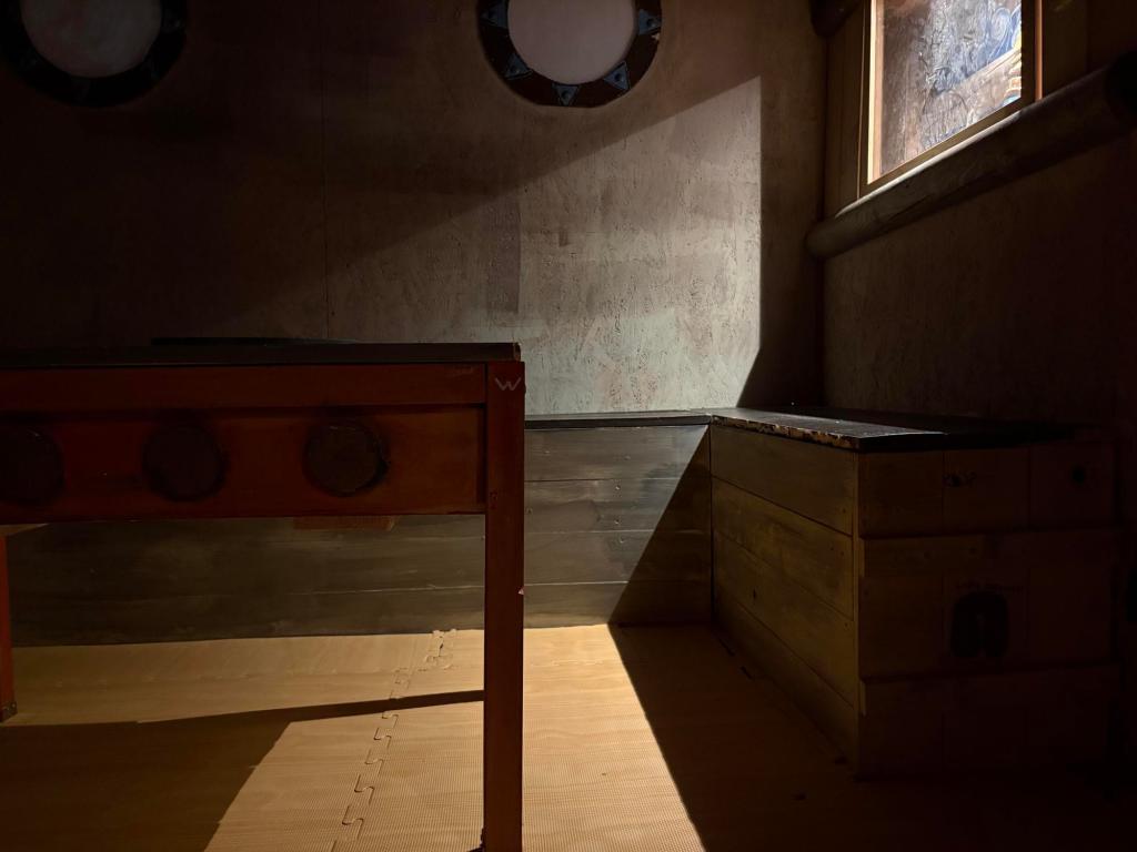 Ship's bridge showing a red table, light coming through a window, and two portholes