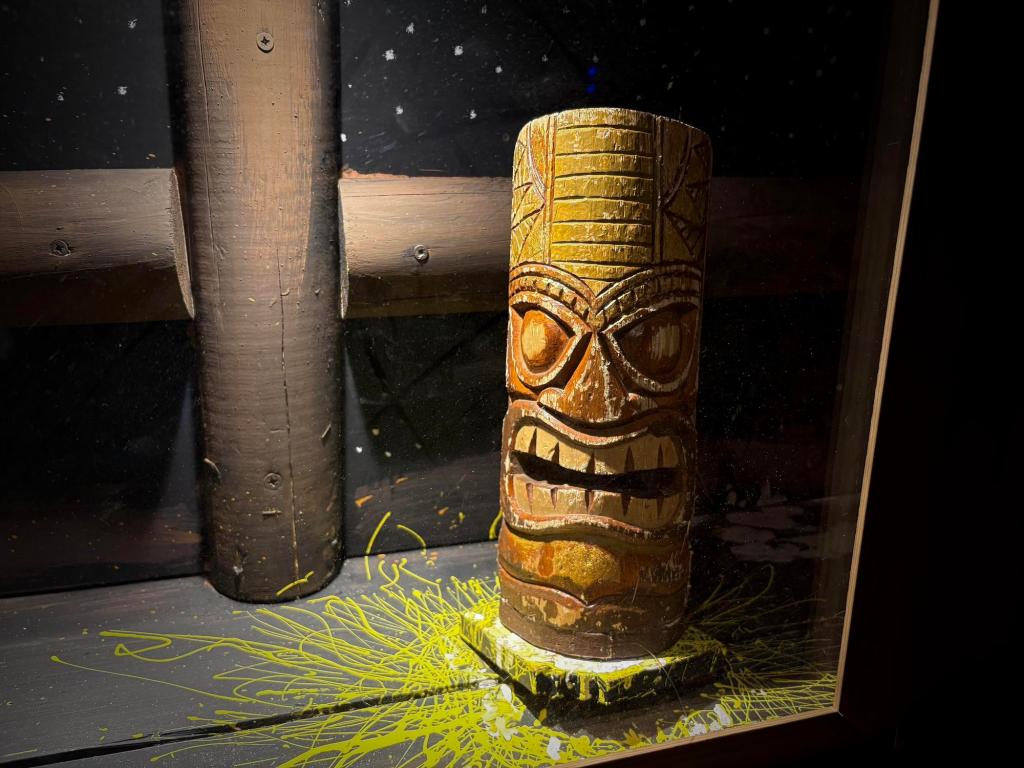 Closeup of a Tiki statue on a board with yellow paint splatters.