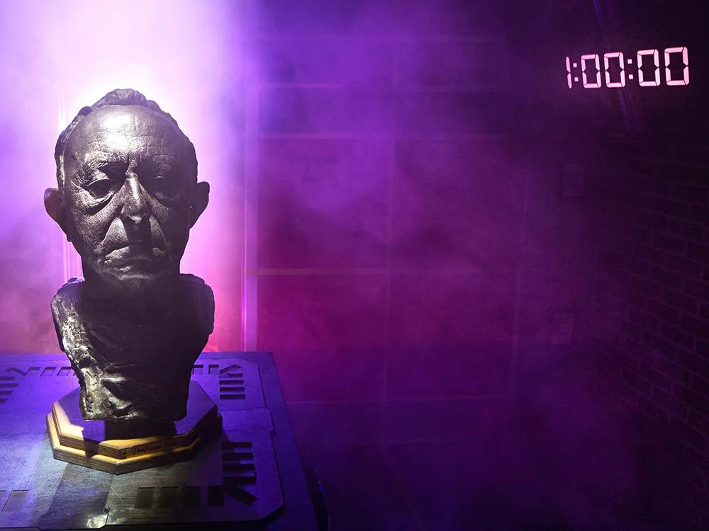 A bronze bust of a man amidst a purple haze with a 1:00:00 display in the background
