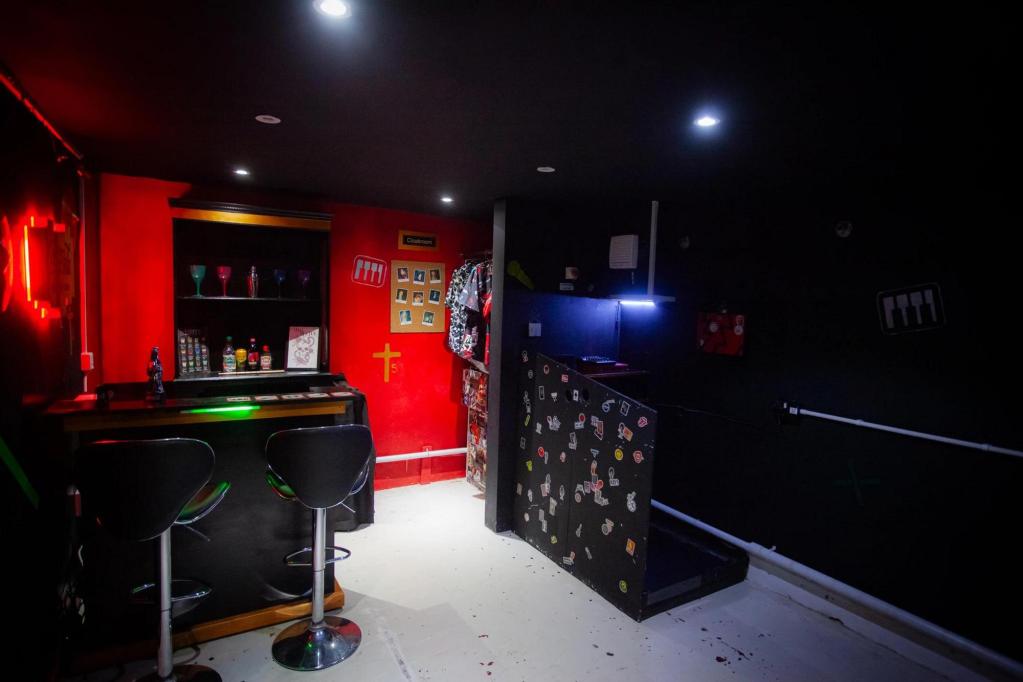 The back half of a grungy music bar, with two stools by a bar and a small sound booth