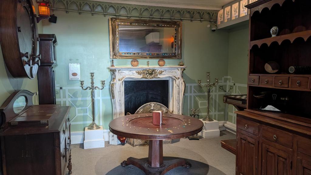 An ornate room with a white fireplace, antique wooden furniture, and pastel green walls