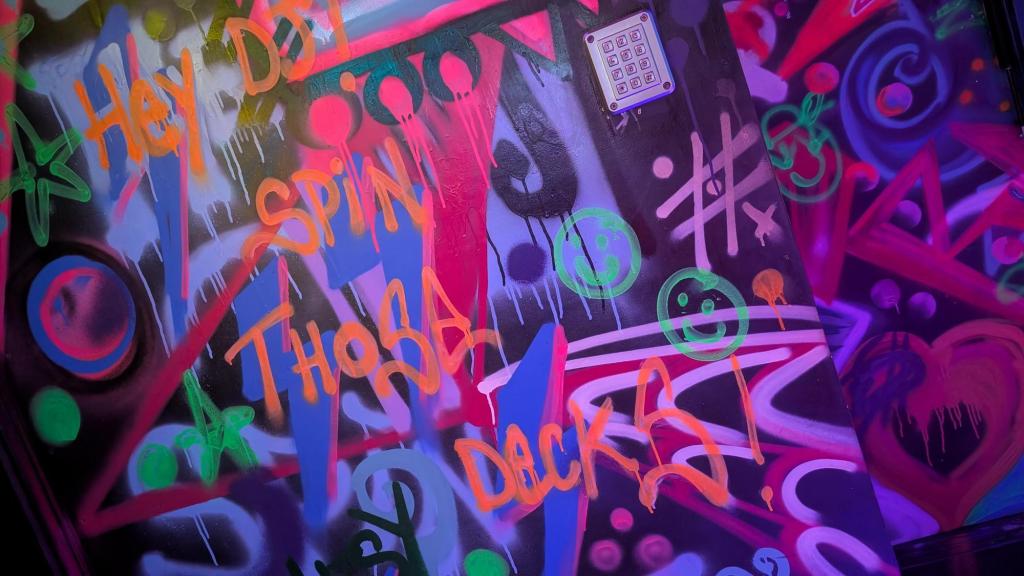 A wall of colorful graffiti with the writing "Hey DJ, spin those decks!"