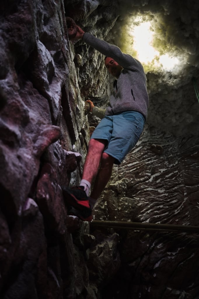 A man descends down a rock face, while light shines through clouds above.
