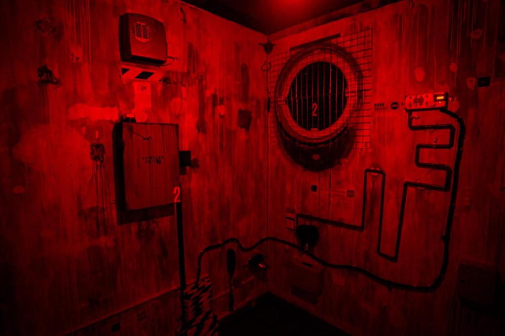 A dimly lit elevator shift with an air vent, various maintenance boxes, and some winding cables