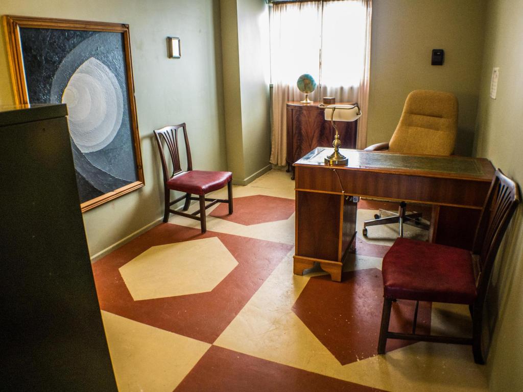An old-school office with a large wooden desk, some chairs, and a grayscale painting on the wall