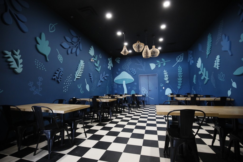 room with lots of tables and chairs, black and white checkered floor, blue walls with leaves and mushroom decorations