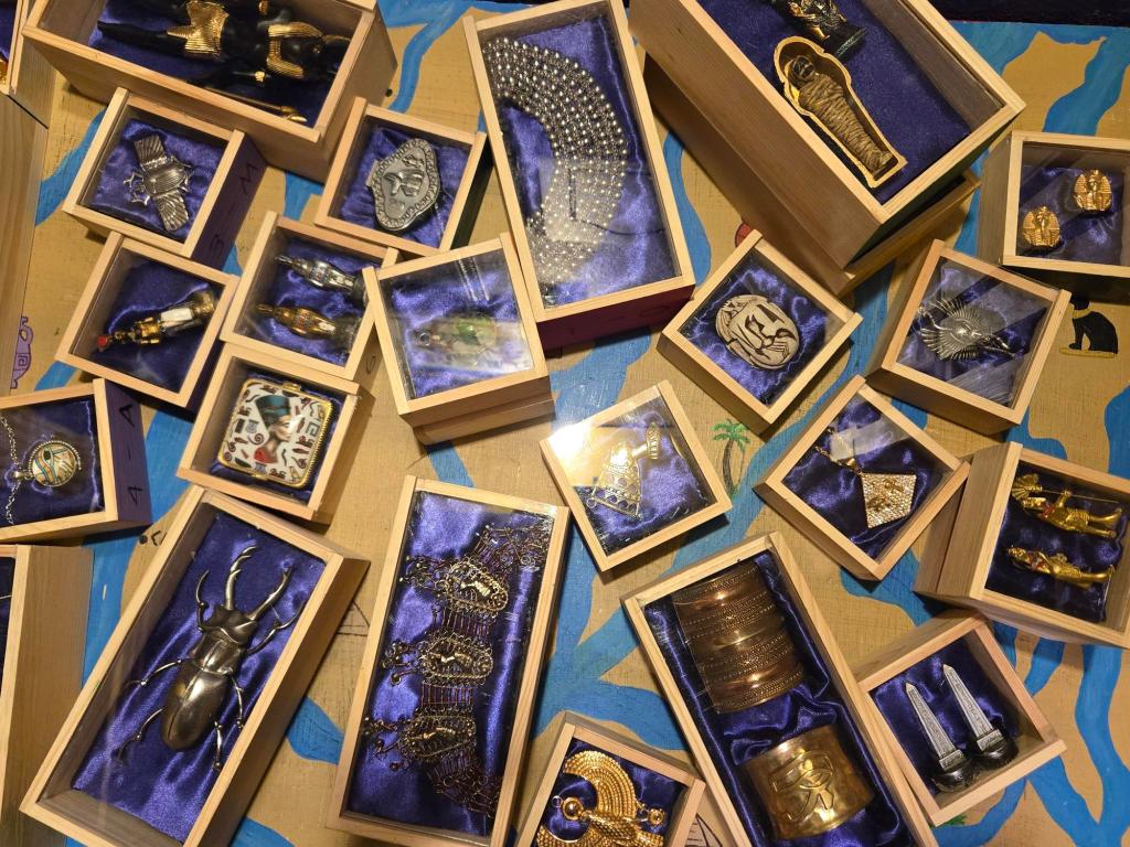 More than a dozen wooden boxes lined with purple cloth laid out on a table. Each box contains different Egyptian baubles and artifacts.