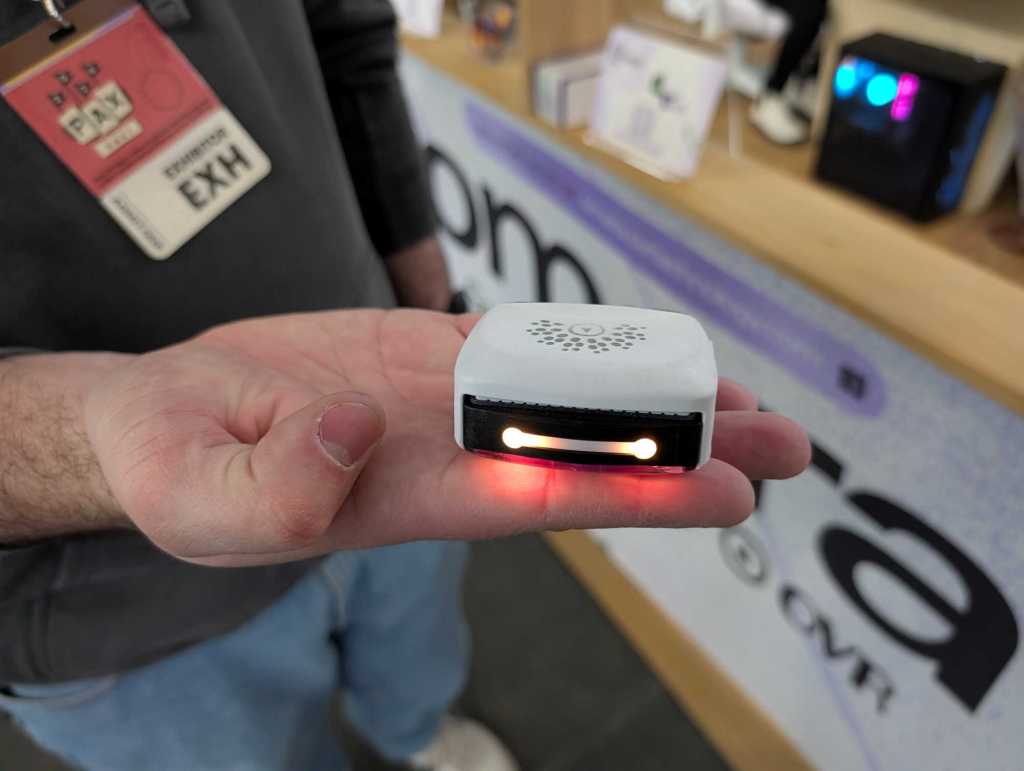 A close up of a hand holding a small white square device with lights on the front.