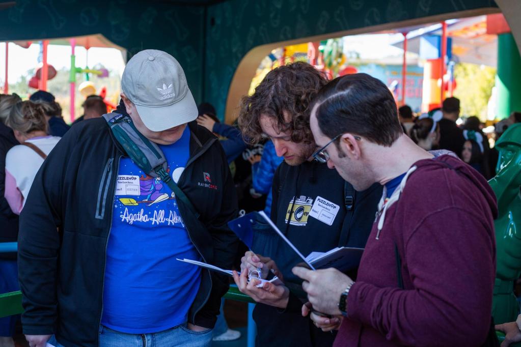 REA contributor Matthew Stein and teammates solving a puzzle in a white binder while waiting in line at Disney