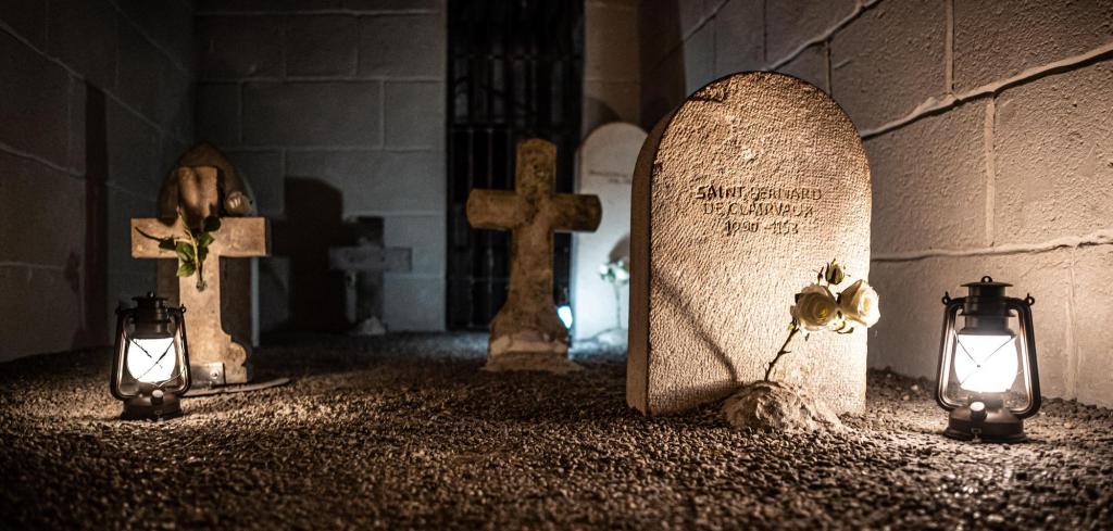 Stone tombstones in a small walled-in graveyard, illuminated by lanterns