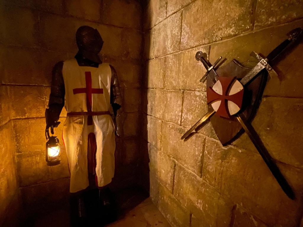 A suit of armor in a Knights Templar tunic at the end of a stone corridor