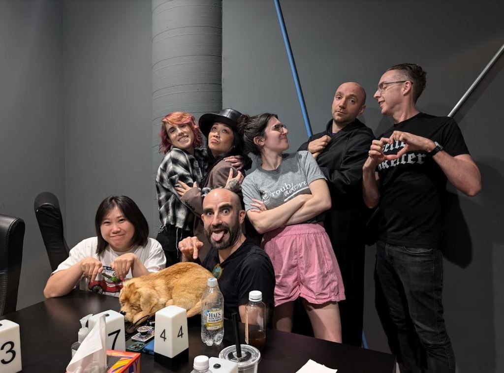 group of friends posing in grey room. Some are hugging, some are glaring, some are kneeling on the ground