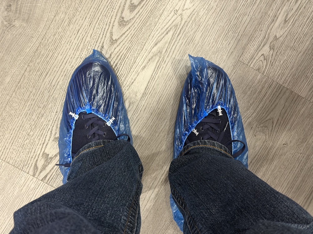Looking down at a pair of shoed feet. The shoes are covered in plastic.