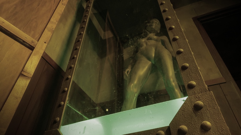 a view upward to a mannequin in a glass case, which is against a wood paneled wall