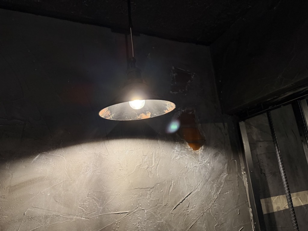 A single metal light fixture hanging in a concrete walled prison cell.