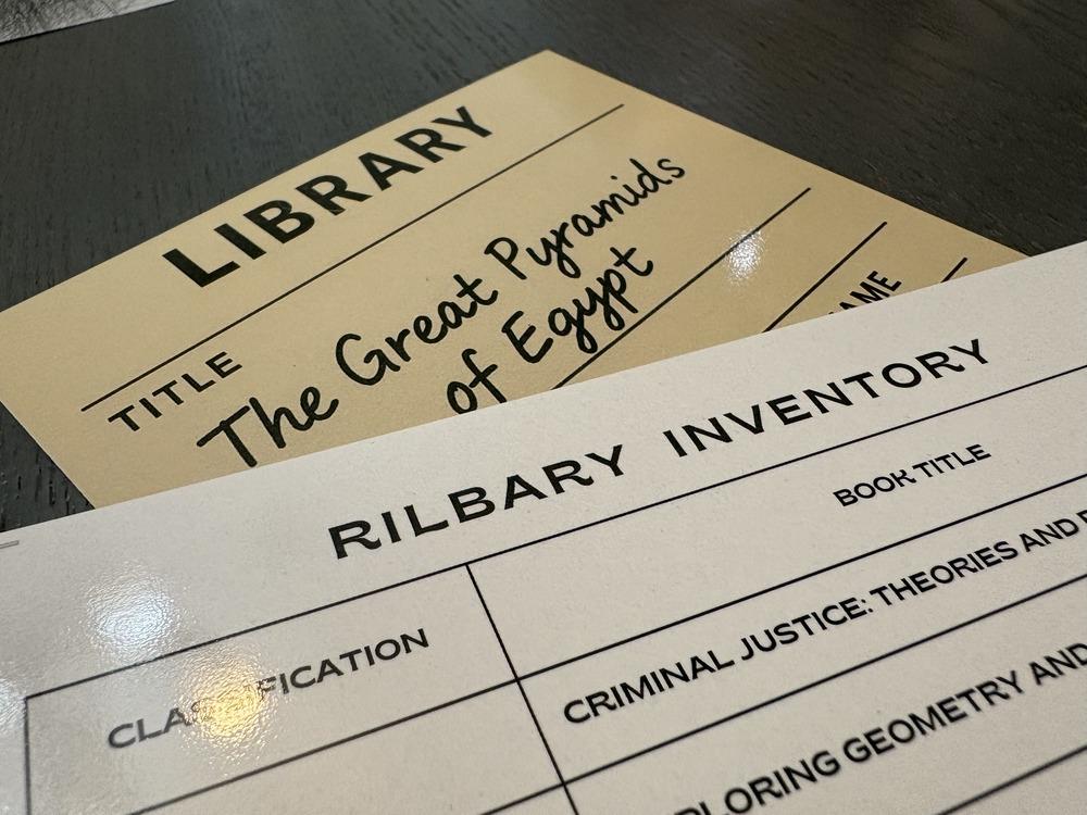 A close up of printed game materials including a library inventory (spelled incorrectly as "rilbary") and a library card