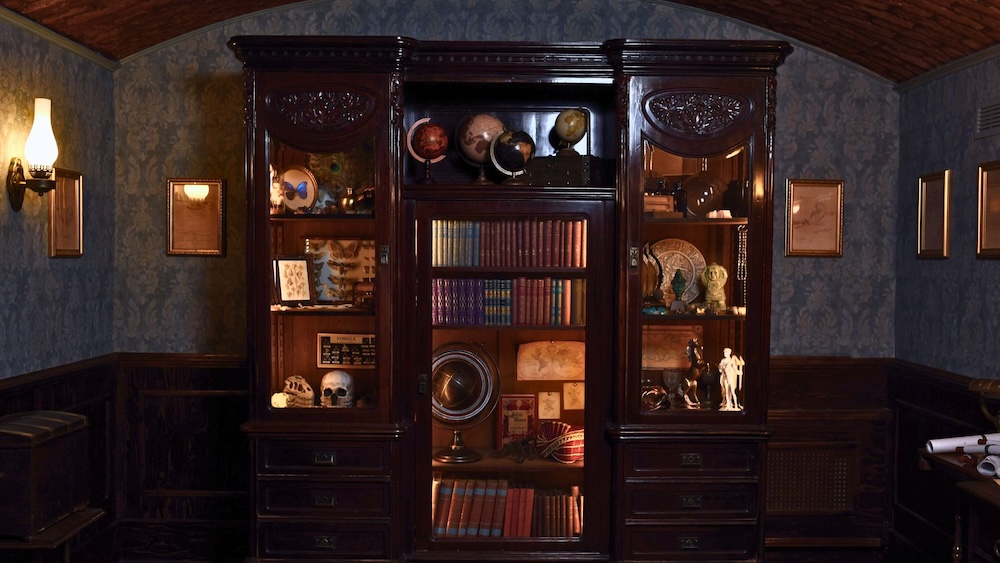 A beautiful bookshelf covered in artifacts from around the world in a Victorian steampunk office.