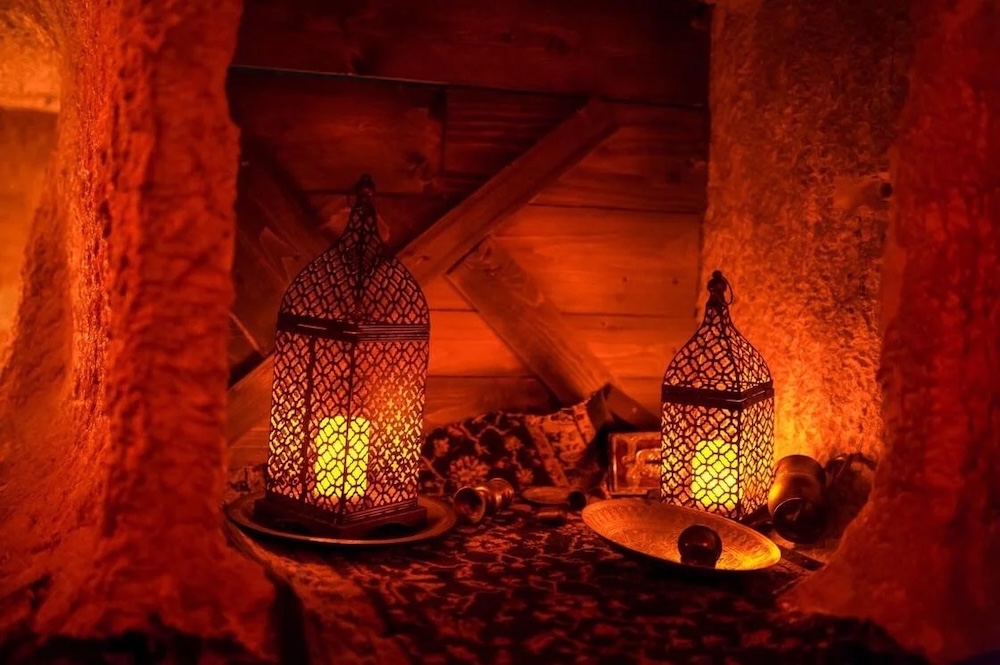 Closeup of a small nook in an ancient Arabian setting. It is lit by shrouded candles atop a carpet.