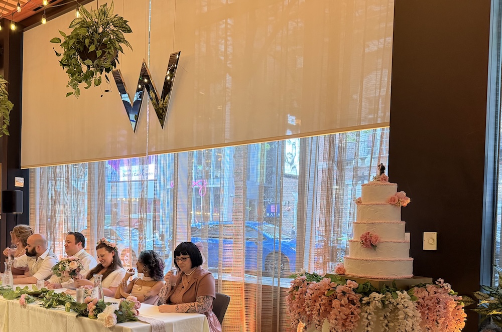 A wedding dais beside a very tall wedding cake inside of the W Hotel in Boston.