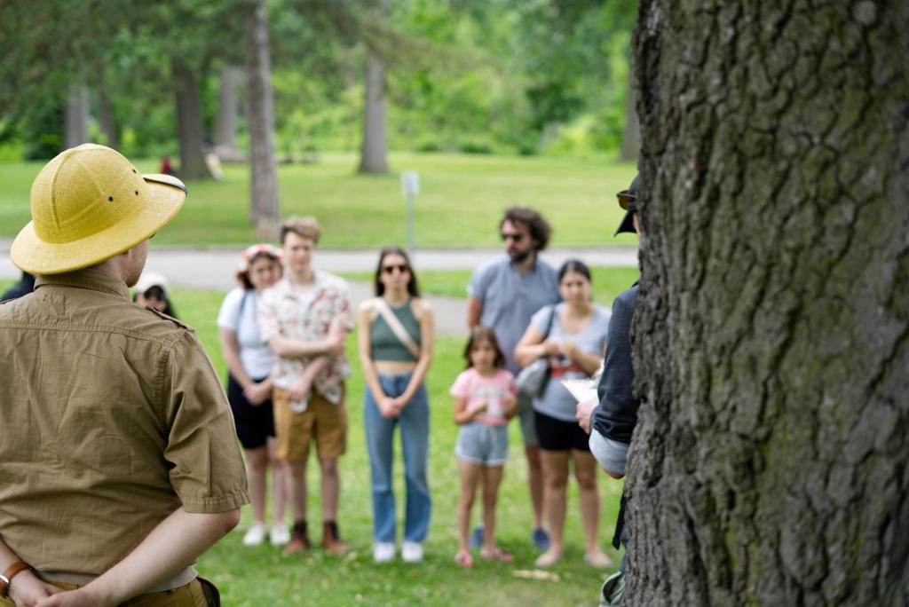 A person in an outdoorsy outfit, standing in front of a group of players in a park
