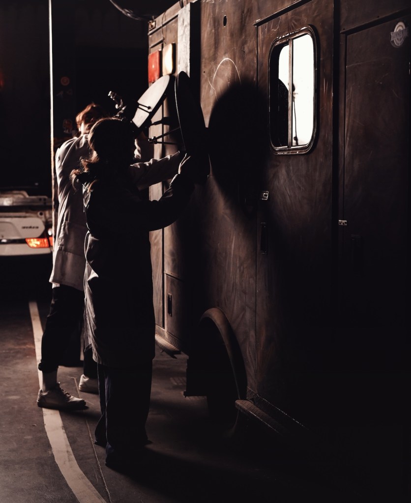 A pair of people manipulating a satellite dish on the side of a truck.