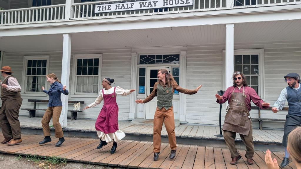 A line of characters dancing in front of The Half Way House