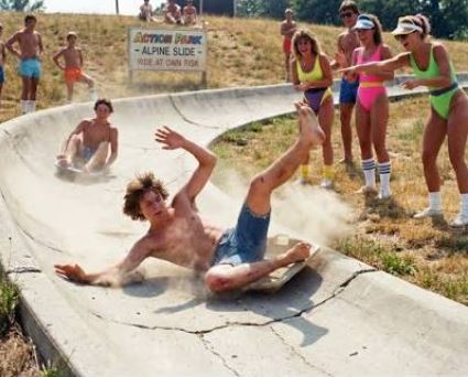 teenagers racing down a concrete pip with women in bright aerobics outfits cheering