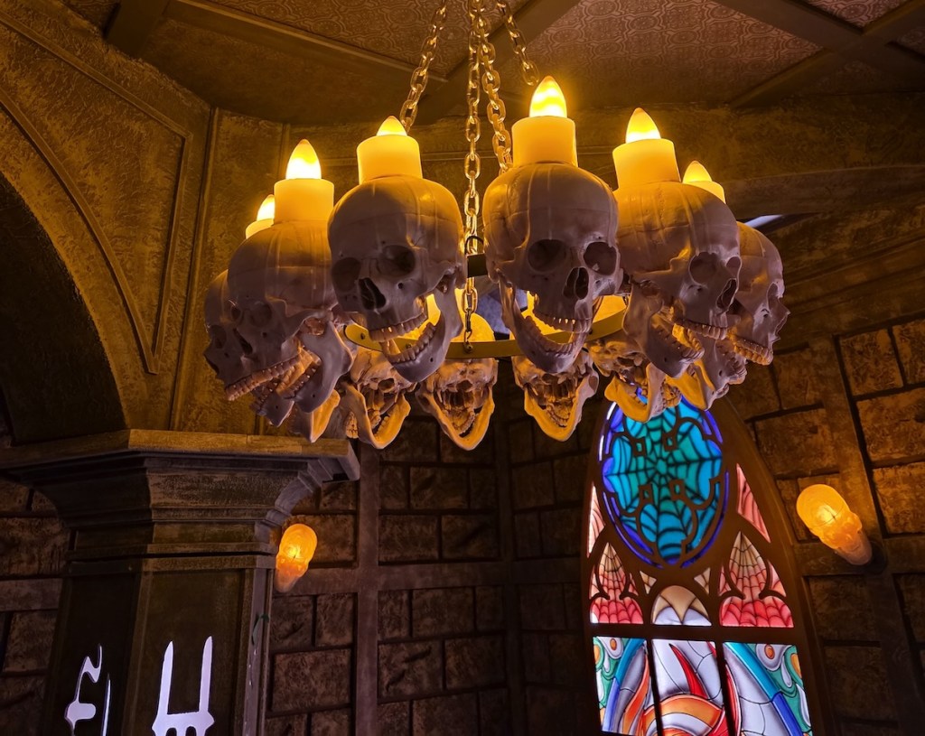 A candelabra made of skulls with glowing candles inside of a castle with stained glass windows.