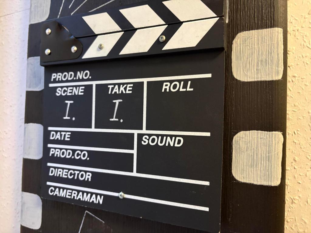 Image of black movie clapboard with white lettering, showing Scene I, Take I, Date, Cameraman, Director and other information