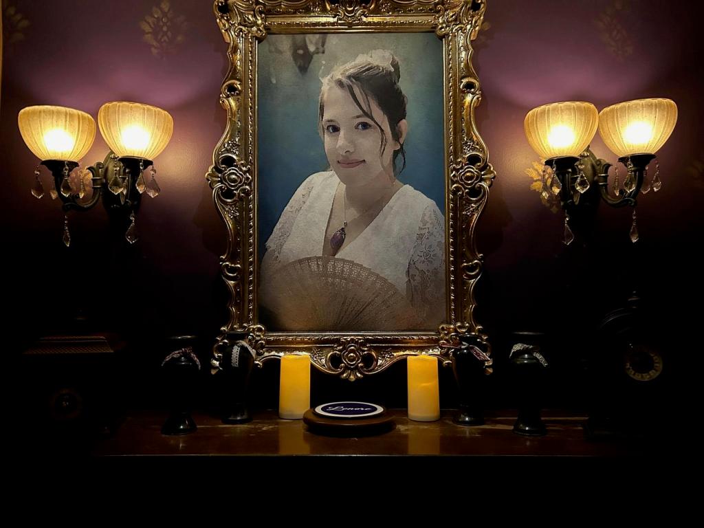 A portrait of a beautiful woman on a wall, over a mantle, surrounded by lamps and candles.