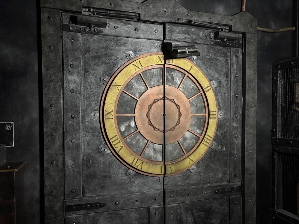 Image of a gray weathered portal, with a large gold and copper clock face showing Roman numerals around the rim.