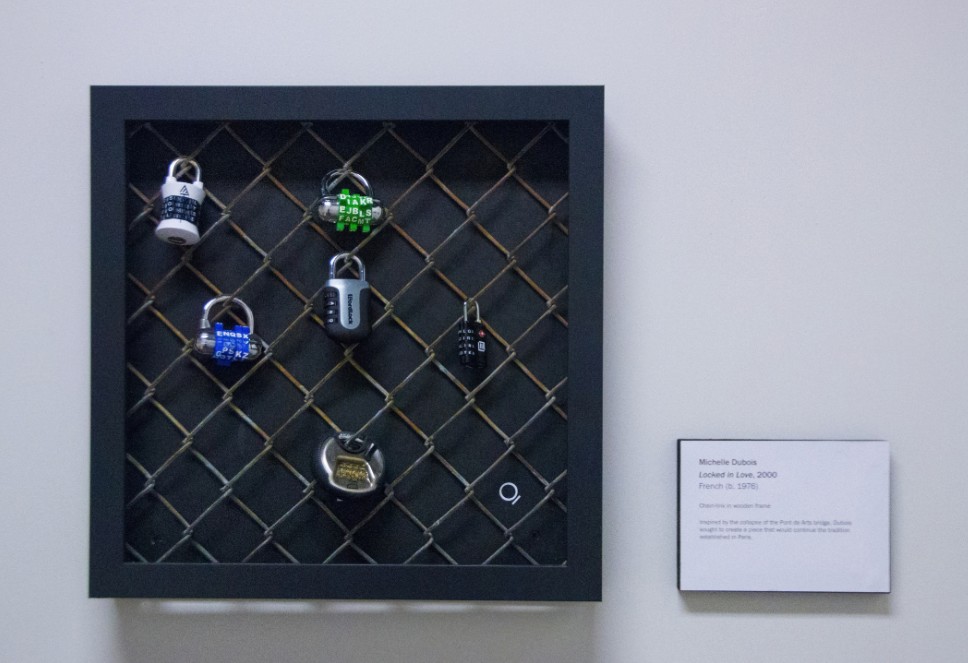 6 different locks attached to segment of chain link fence framed in an art gallery